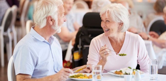 Senior Couple Eating Meal And Talking In Retirement Home
