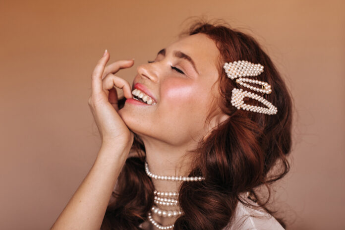 positive-woman-with-curly-hair-laughs-bites-her-finger-portrait-woman-with-white-hairpins-pearl-necklace