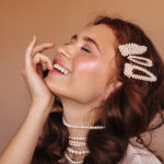 positive-woman-with-curly-hair-laughs-bites-her-finger-portrait-woman-with-white-hairpins-pearl-necklace