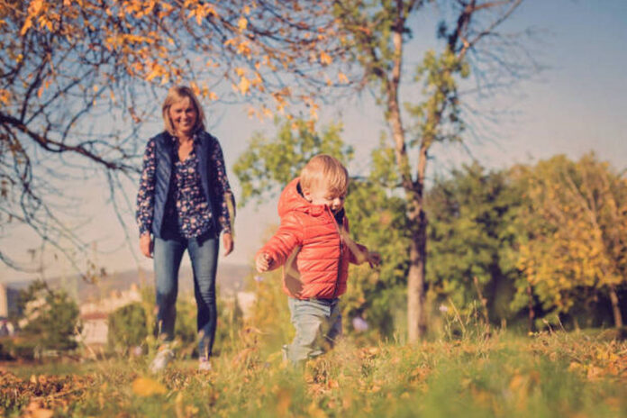 Happy grandmother playing with baby grandson in public park in autumn